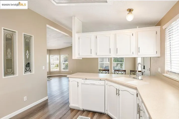 Kitchen featuring healthy amount of natural light, white dishwasher, dark wood finished floors, white cabinets, and a textured ceiling