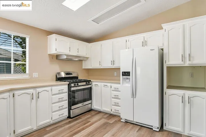 Kitchen with white refrigerator with ice dispenser, gas stove, lofted ceiling, white cabinetry, and a textured ceiling