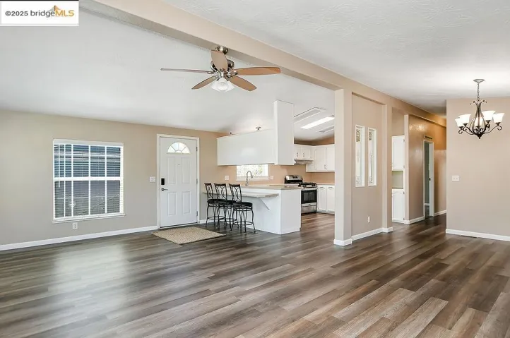 Unfurnished living room featuring a chandelier, dark wood-style flooring, a ceiling fan, and a textured ceiling