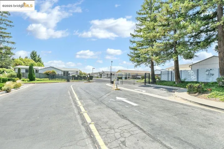 View of asphalt street featuring a residential view, curbs, sidewalks, a gated entry, and a gate