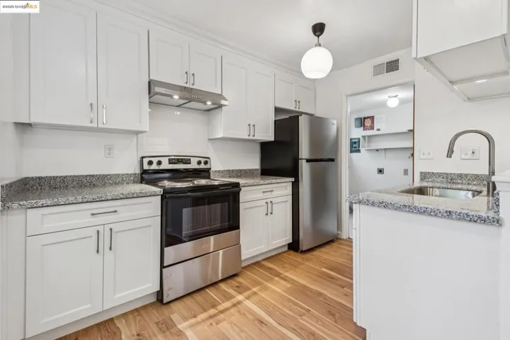 Kitchen featuring appliances with stainless steel finishes, light wood-type flooring, under cabinet range hood, and white cabinets