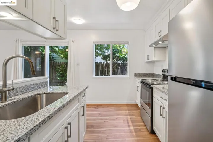 Kitchen with appliances with stainless steel finishes, light wood-type flooring, under cabinet range hood, white cabinets, and light stone counters