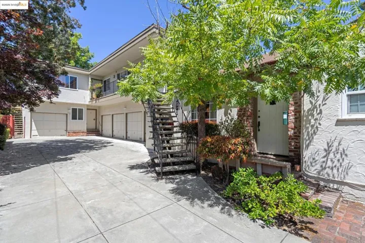 View of property hidden behind natural elements featuring an attached garage, stucco siding, driveway, and stairs