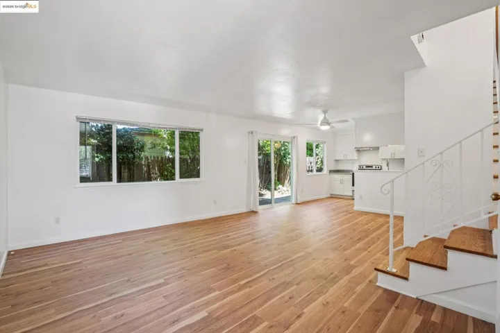 Unfurnished living room with stairs, light wood-style floors, and a ceiling fan