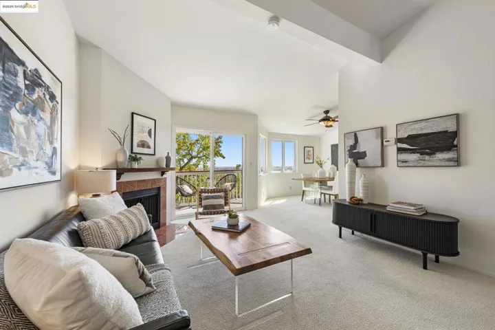 Carpeted living area with a tiled fireplace, a ceiling fan, and beamed ceiling