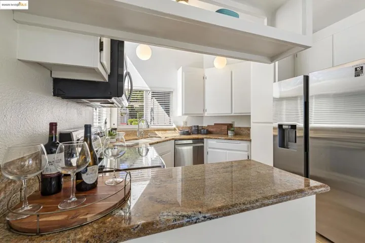 Kitchen with stainless steel appliances, white cabinetry, and stone counters