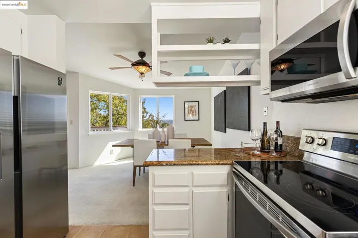 Kitchen with stainless steel appliances, light colored carpet, white cabinetry, a peninsula, and dark stone countertops