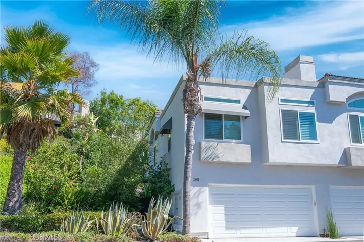 This inviting end unit sits beside a lush greenbelt and features a beautifully landscaped front garden, with vibrant greenery and flowering plants that frame the home's charming exterior.