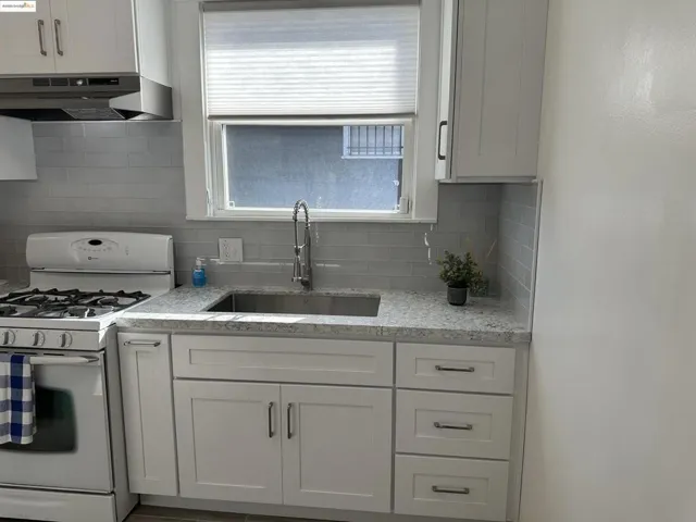 Kitchen with white range with gas cooktop, under cabinet range hood, backsplash, and white cabinetry
