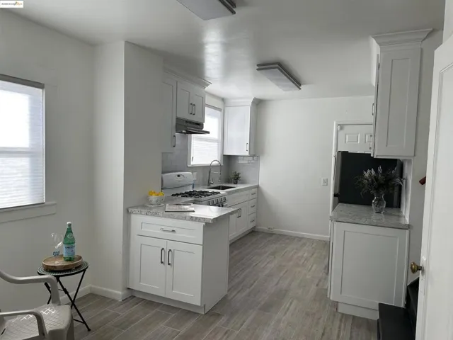 Kitchen featuring light wood-style floors, tasteful backsplash, white gas stove, white cabinetry, and under cabinet range hood