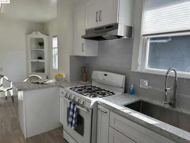 Kitchen featuring gas range gas stove, tasteful backsplash, under cabinet range hood, white cabinets, and wood finished floors