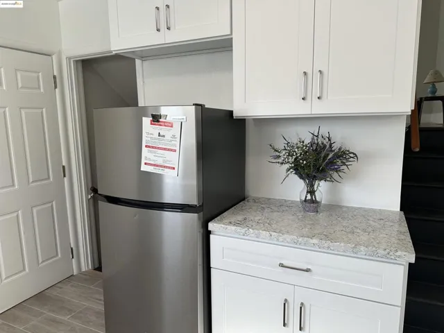 Kitchen with freestanding refrigerator, white cabinetry, light stone countertops, and wood finish floors
