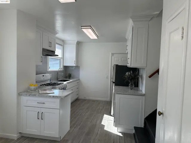 Kitchen with white cabinetry, gas range gas stove, wood finished floors, backsplash, and a peninsula