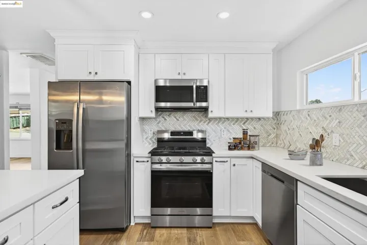 Kitchen featuring appliances with stainless steel finishes, light countertops, white cabinetry, light wood-style flooring, and recessed lighting