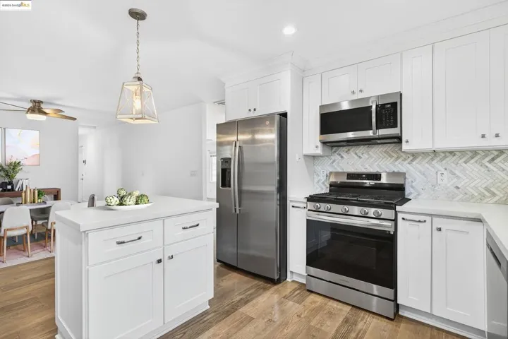 Kitchen featuring appliances with stainless steel finishes, backsplash, light countertops, a ceiling fan, and light wood finished floors