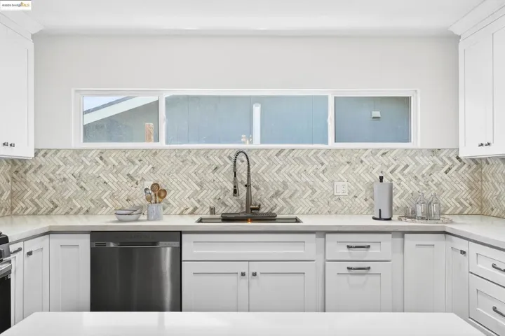 Kitchen with stainless steel dishwasher, decorative backsplash, white cabinetry, and light countertops