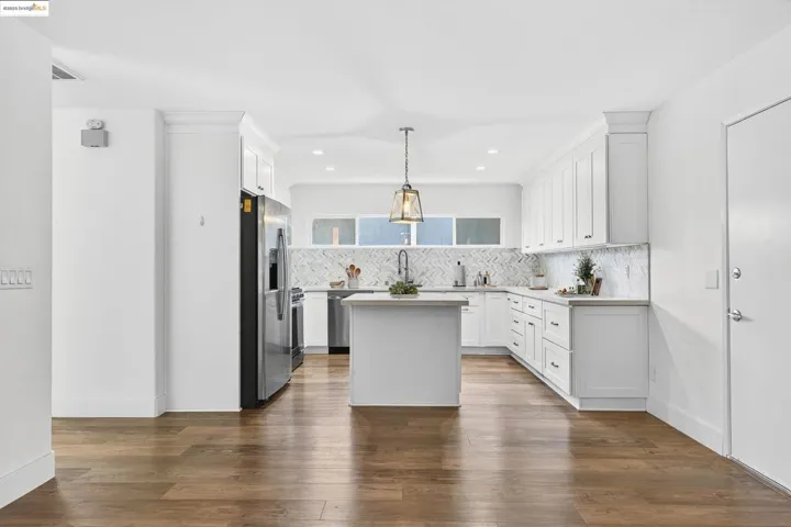 Kitchen featuring light countertops, a kitchen island, dark wood-type flooring, stainless steel appliances, and decorative backsplash