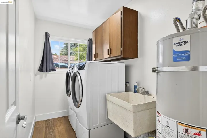 Laundry area with cabinet space, washing machine and clothes dryer, water heater, and wood finished floors