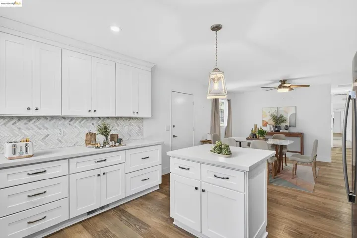 Kitchen with ceiling fan, dark wood-type flooring, backsplash, light countertops, and hanging light fixtures