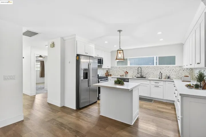 Kitchen with appliances with stainless steel finishes, backsplash, light countertops, wood finished floors, and white cabinets
