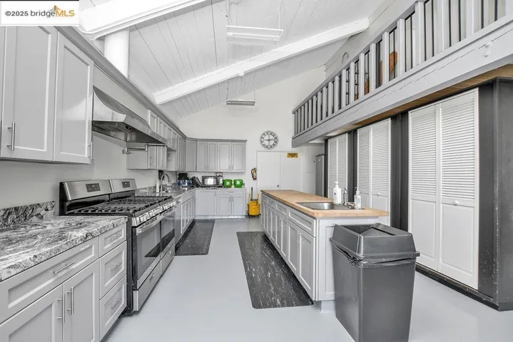 Kitchen with stainless steel range with gas cooktop, beam ceiling, high vaulted ceiling, concrete flooring, and wall chimney range hood