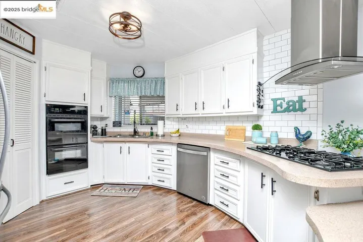 Kitchen featuring wall chimney range hood, backsplash, white cabinets, and light wood-style flooring