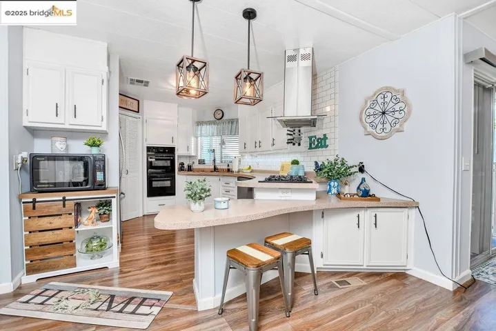 Kitchen with a peninsula, backsplash, white cabinetry, island range hood, and a kitchen breakfast bar