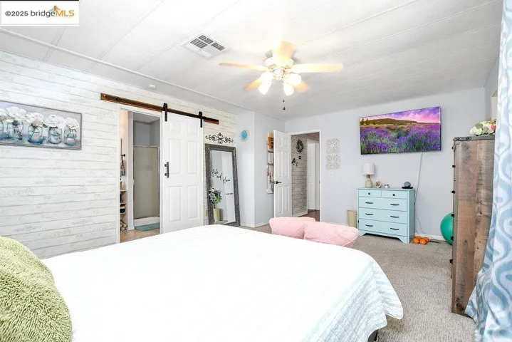 Carpeted bedroom featuring a barn door, wood walls, and a ceiling fan