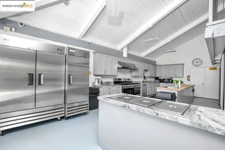 Kitchen with beamed ceiling, gray cabinetry, concrete floors, appliances with stainless steel finishes, and high vaulted ceiling