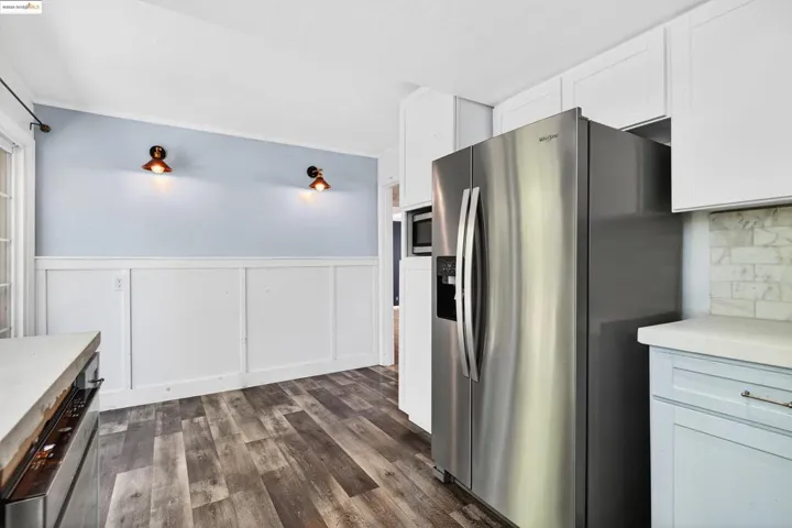 Kitchen with a decorative wall, appliances with stainless steel finishes, wainscoting, dark wood-style flooring, and white cabinets