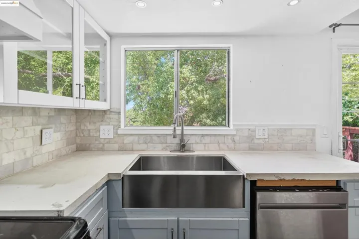 Kitchen featuring dishwashing machine, plenty of natural light, gray cabinets, and custom range hood