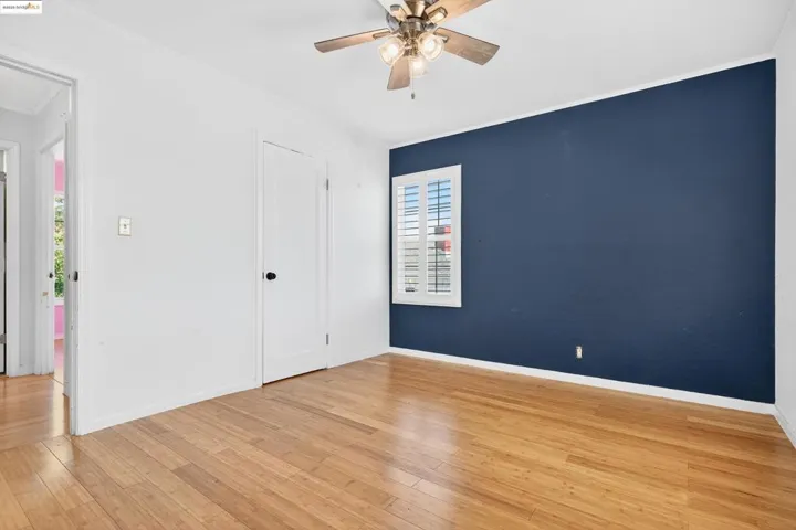 Unfurnished bedroom with light wood-style floors, ornamental molding, attic access, and ceiling fan