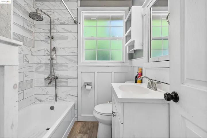Bathroom with vanity, wood finished floors, bathing tub / shower combination, healthy amount of natural light, and a decorative wall