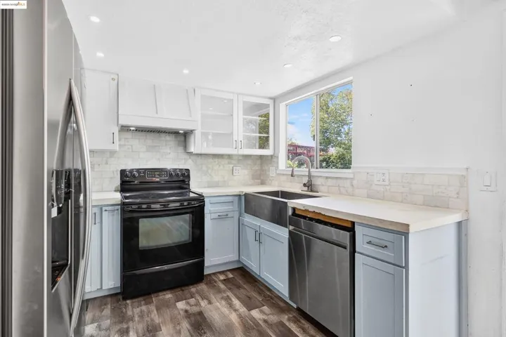 Kitchen featuring stainless steel appliances, dark wood-style flooring, custom range hood, backsplash, and white cabinets