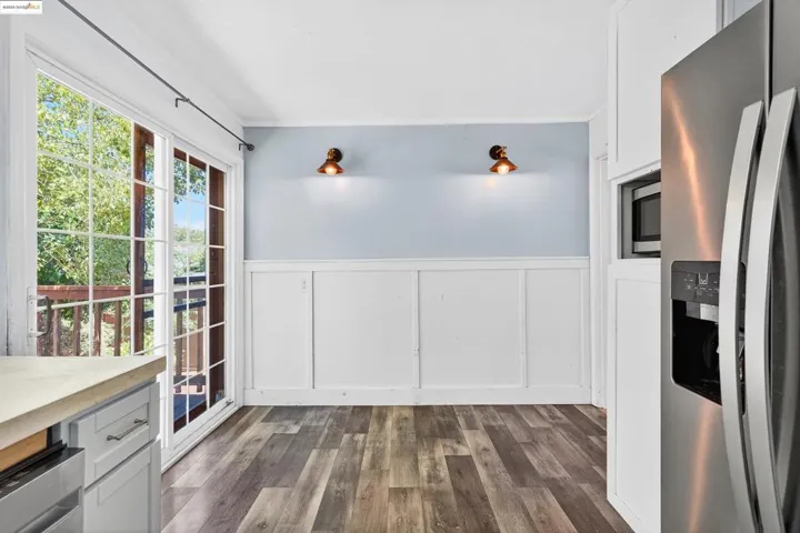 Kitchen with appliances with stainless steel finishes, a decorative wall, wainscoting, dark wood-type flooring, and light countertops