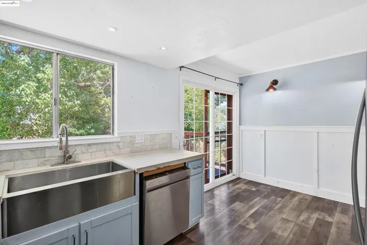 Kitchen featuring a decorative wall, stainless steel appliances, a wainscoted wall, light countertops, and dark wood-style floors