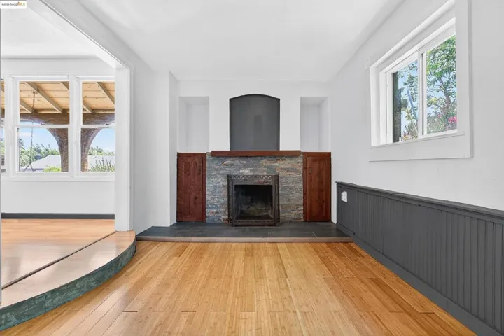Unfurnished living room featuring a stone fireplace, light wood finished floors, and wainscoting