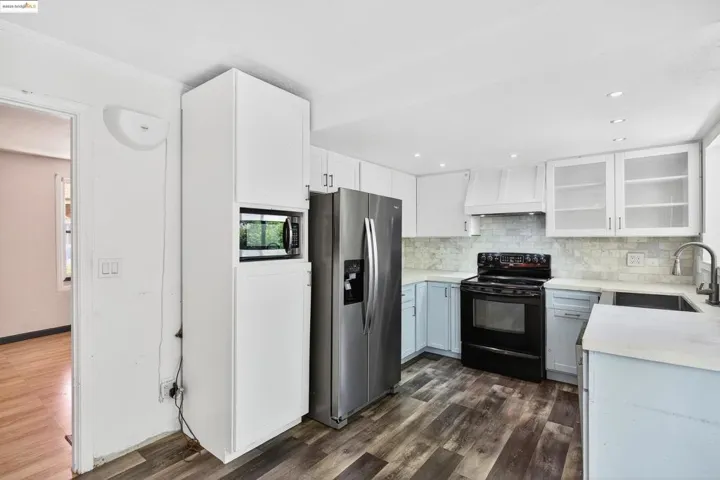 Kitchen featuring stainless steel appliances, light countertops, custom exhaust hood, white cabinetry, and dark wood-type flooring