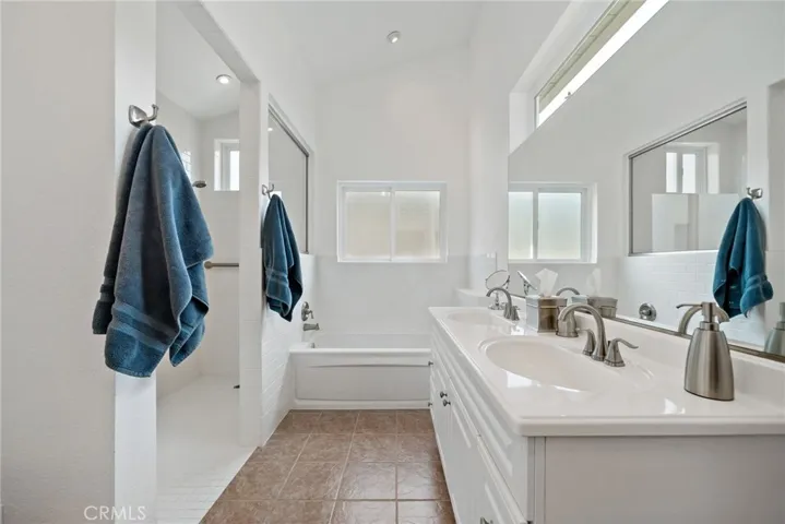 Primary bathroom tiled flooring, dual sinks, walk-in shower to left and separate tub