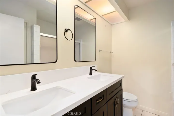The redesigned hall bath showcases dual sinks, a modern vanity with quartz counters, stylish fixtures, and a linen closet for extra storage.