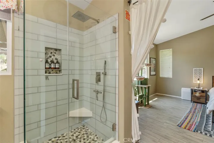Spa-like tiled walk-in shower with fixtures and a large showerhead, glass door, corner seat, and built-in niche for shampoo, conditioner, and shower gels.