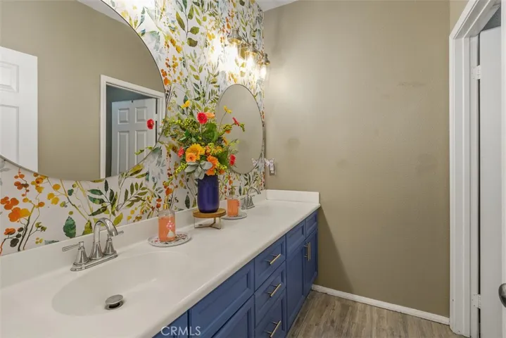 The secondary bathroom features a dual-sink vanity, stylish round mirrors, and floral wallpaper.