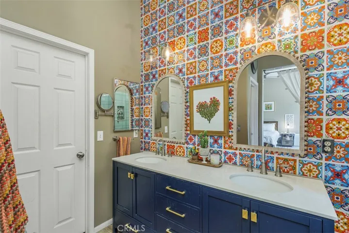Stylish wallpaper, dual-sink vanity with gold knobs and handles, mirrors, and access to the walk-in closet.