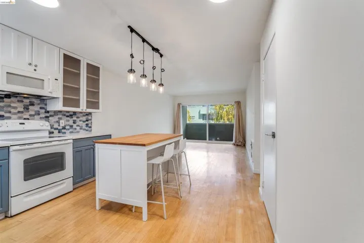 Two tone kitchen featuring white appliances, two tone cabinetry, a breakfast bar, glass insert cabinets, and butcher block countertops