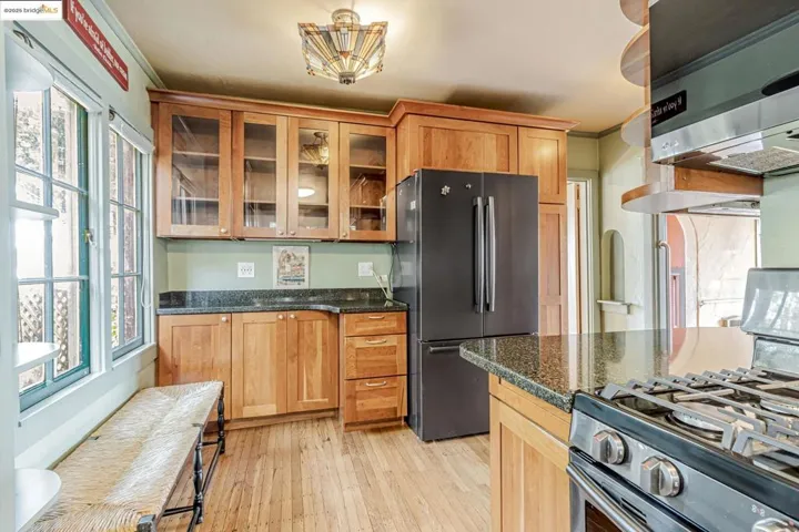 Kitchen with gas stove, glass insert cabinets, freestanding refrigerator, light wood-type flooring, and dark stone counters