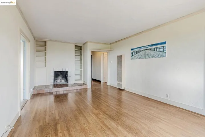 Unfurnished living room with built in features, light wood-style flooring, a fireplace with raised hearth, a heating unit, and ornamental molding