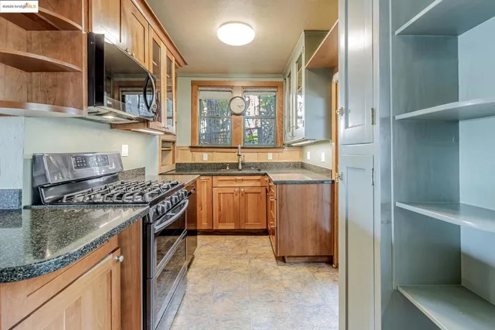 Kitchen with stainless steel appliances, open shelves, brown cabinetry, and dark stone counters