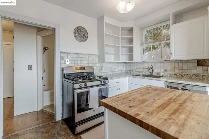Kitchen with wooden counters, stainless steel appliances, open shelves, white cabinetry, and backsplash