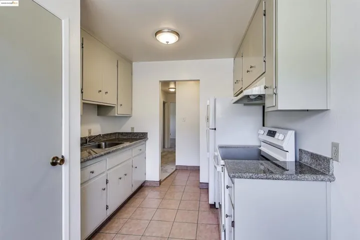 Kitchen with white range, light tile patterned flooring, and under cabinet range hood