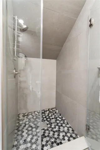 Contemporary walk-in shower with frameless glass doors, premium fixtures, and pebble tile flooring.